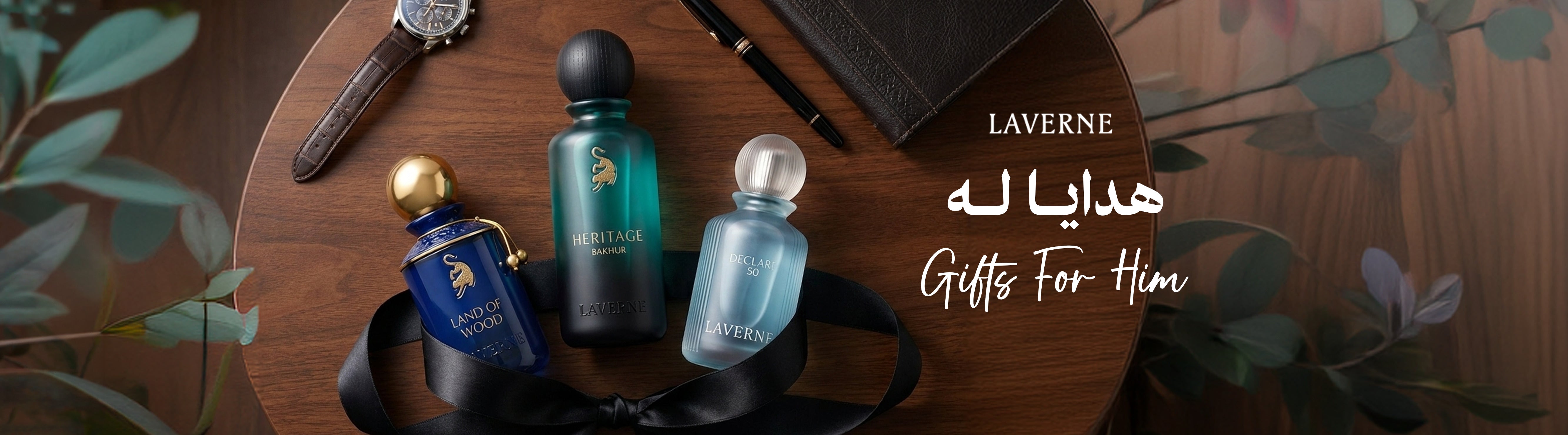 A curated flat lay of Laverne men's perfumes, including Land of Wood and Heritage Bakhur, arranged on a wooden table with a leather wallet, pen, and watch, featuring the text "Gifts For Him".