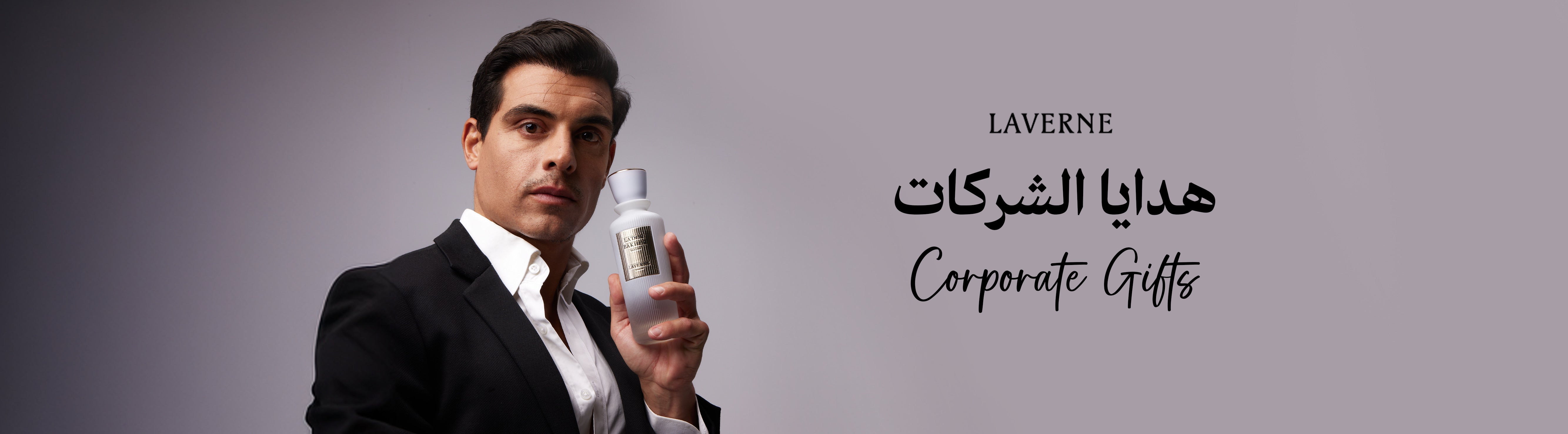 A professional man in a black suit holding a luxury Laverne perfume bottle against a grey background, featuring the text "Corporate Gifts".