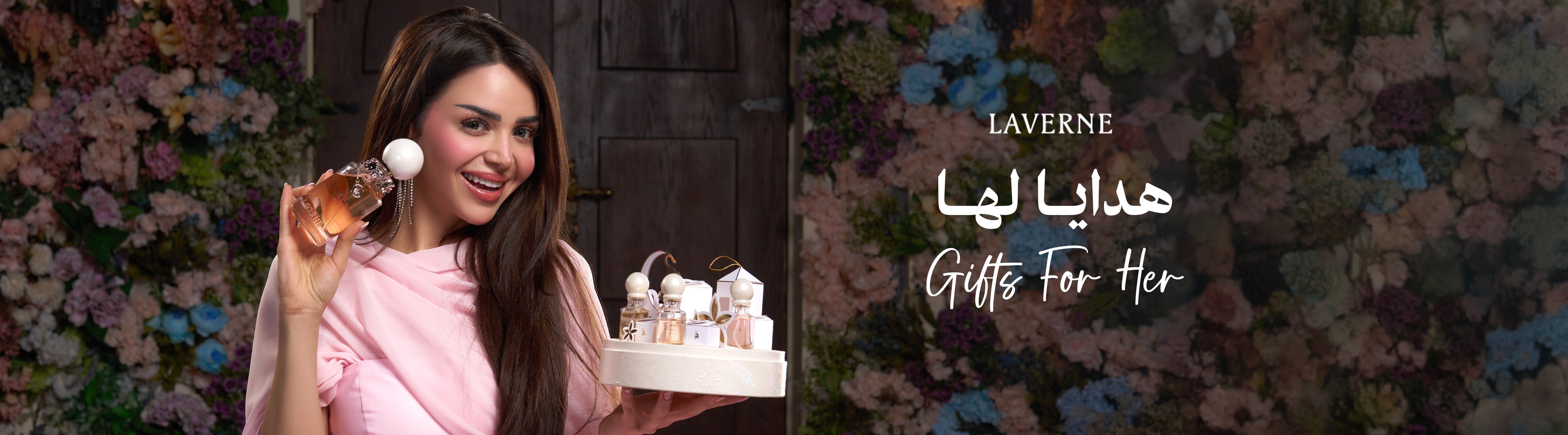 A smiling woman in pink holding a Laverne perfume bottle and a gift set against a floral background, featuring the text "Gifts For Her".